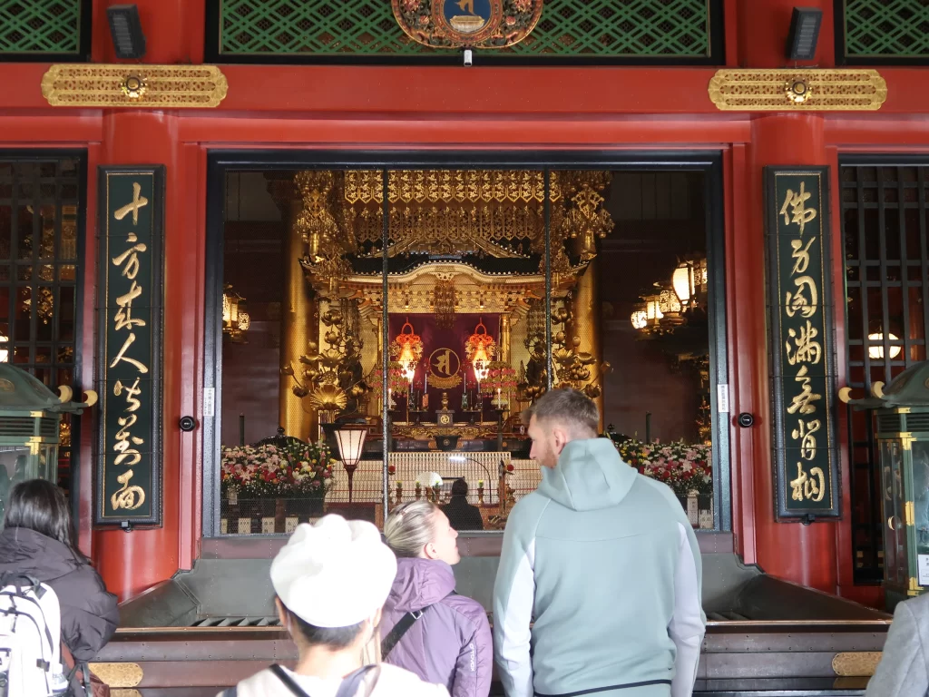 Inside Sensoji Temple main hall showing golden altar and visitors praying in Asakusa Tokyo Japan