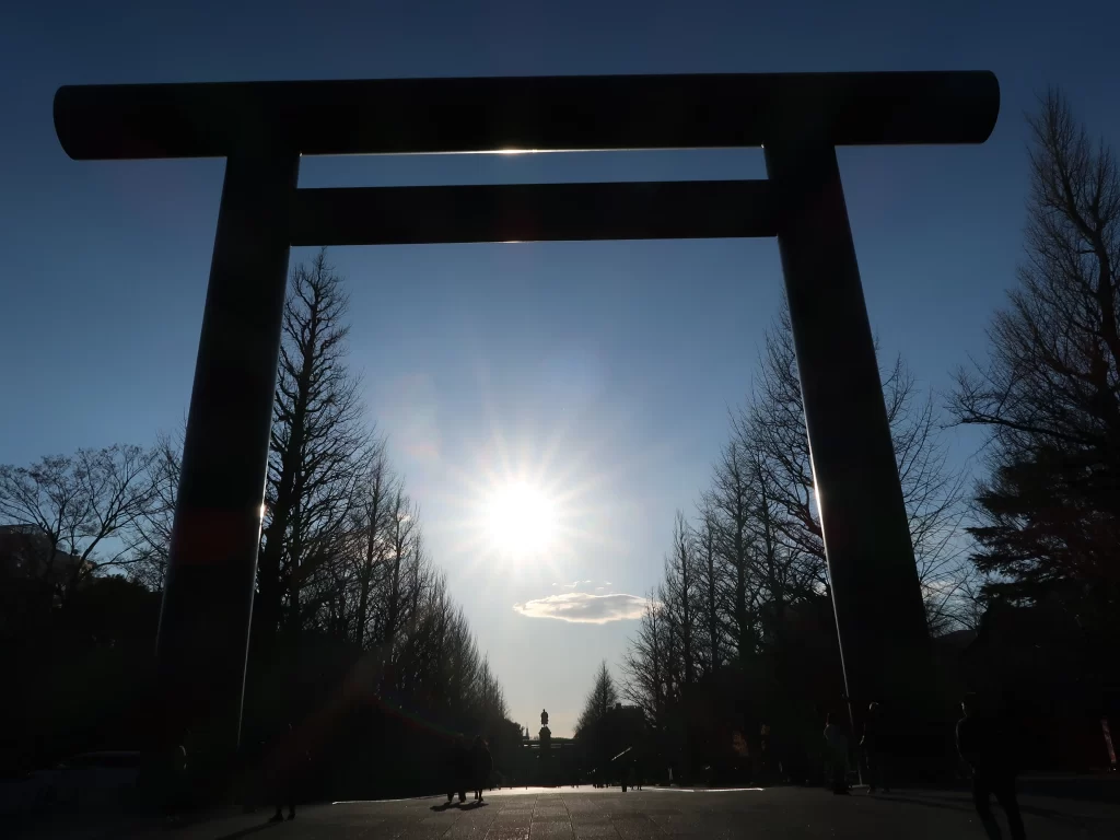 Yasukuni Shrine torii gate in Tokyo with the sun shining through, creating a dramatic silhouette view along the main approach